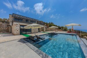 Modern luxury villa with infinity pool, sun loungers and umbrellas, offering stunning ocean views.